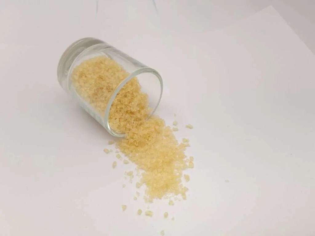 Golden gelatin granules spilling from a tipped glass jar.